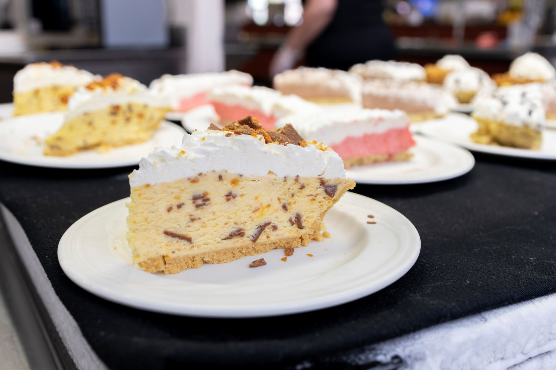 Close-up of various slices of creamy cheesecakes on white plates, displayed on a countertop in a restaurant